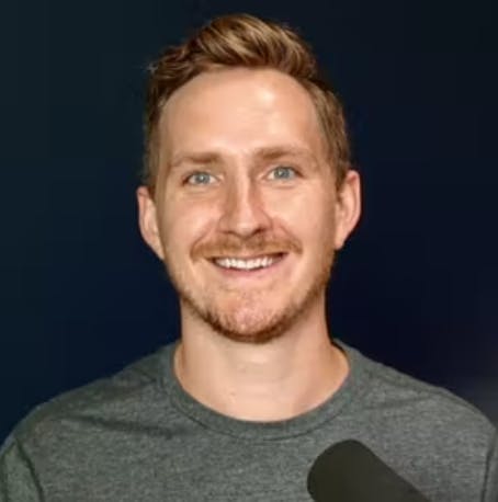 Headshot of Alban Brooke against black background with a podcast mic in front of him